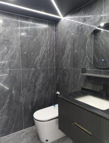 Moderne Badezimmerausstattung mit grauen Fliesen, rotem Waschtisch und beleuchtetem Spiegel.