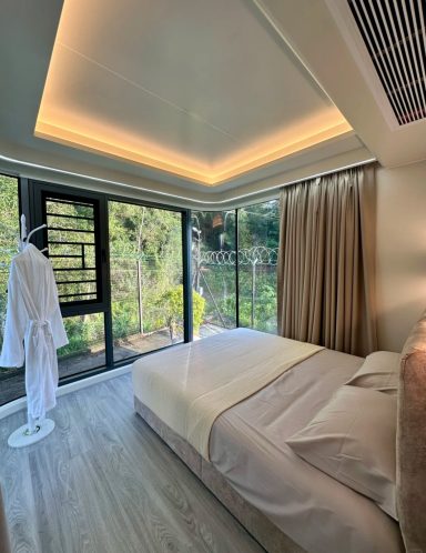 Helles Schlafzimmer mit einem großen Fenster, Sicht auf Natur und komfortabler Einrichtung.