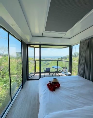 Helles Schlafzimmer mit Blick auf die Natur durch große Fenster. Minimalistische Einrichtung.