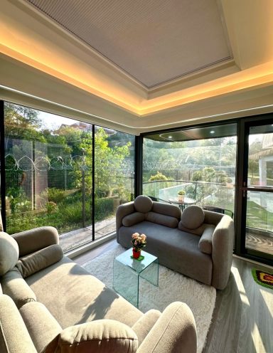 Helles Wohnzimmer mit Blick auf den Garten, bequemen Möbeln und einem Glastisch.